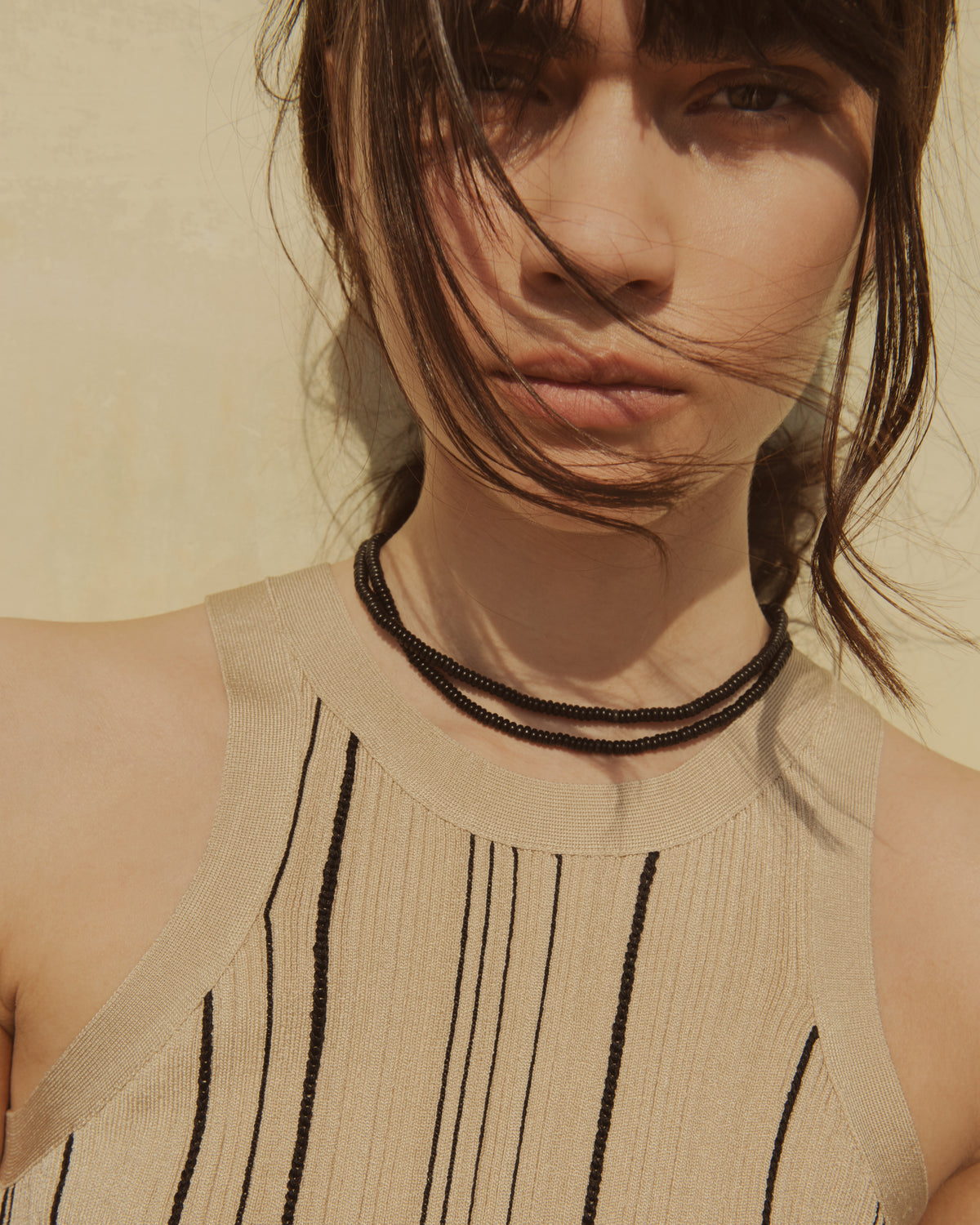 Woman wearing a beige sleeveless top with black stripes against a neutral background